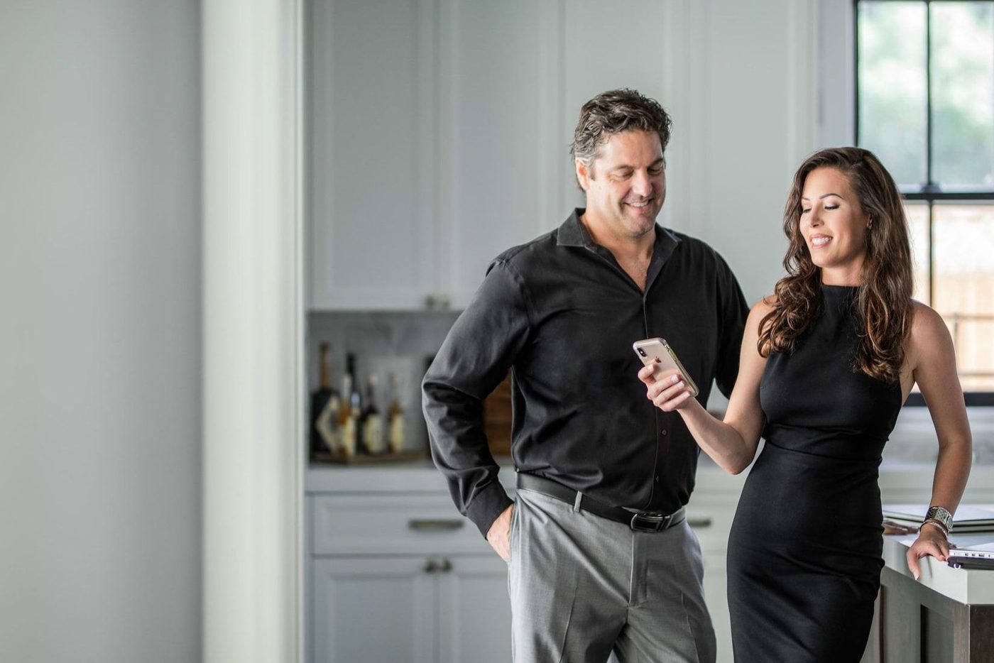 Couple in black outfits looking at phone in a bright kitchen