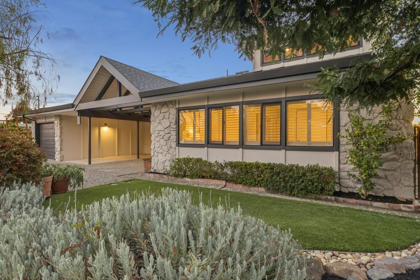 Mid-century modern home with large windows and lush landscaping at dusk