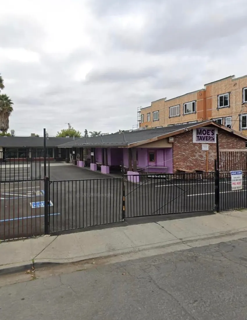 Purple commercial building with Moe's Tavern sign behind black fence